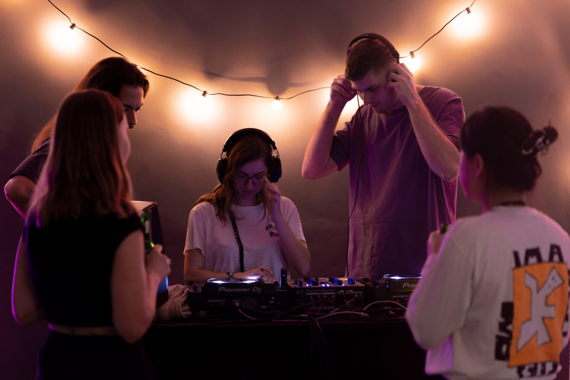 Mehrere Personen stehen um ein DJ-Pult herum.