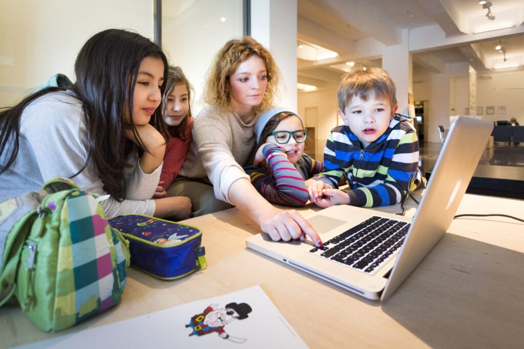 Eine Frau und mehrere Kinder schauen gemeinsam in einen Laptop