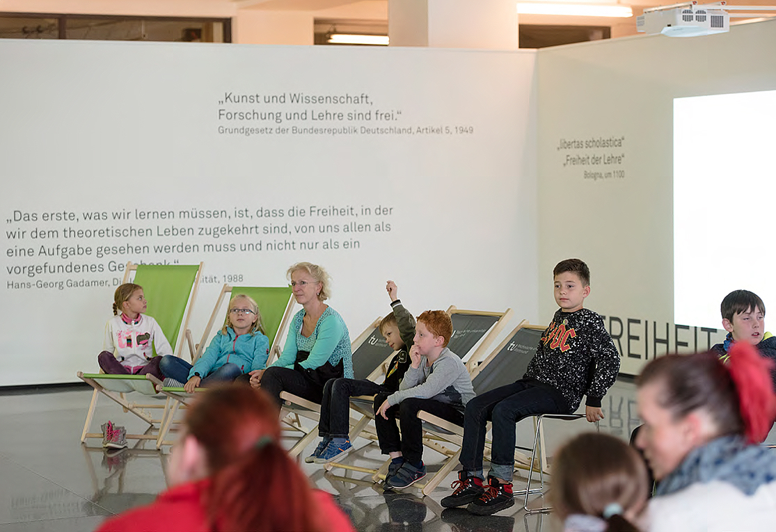 Schülerinnen und Schüler sitzen auf Liegestühlen im weiten Raum bei einer KinderUni-Veranstaltung auf dem Campus Stadt
