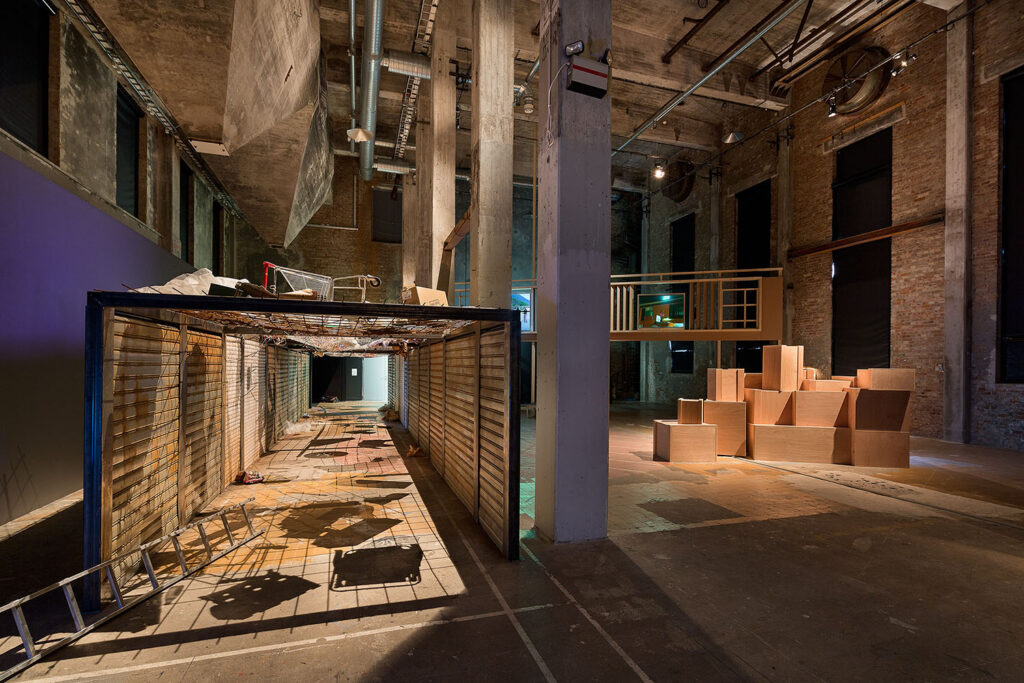 Los de arriba y los de abajo (2015) von Kader Attia: Ein schmaler Gittergang mit Müll über den Köpfen der Besucher*innen verweist auf reale Schutznetze in Hebron und thematisiert Machtverhältnisse sowie soziale Hierarchien.