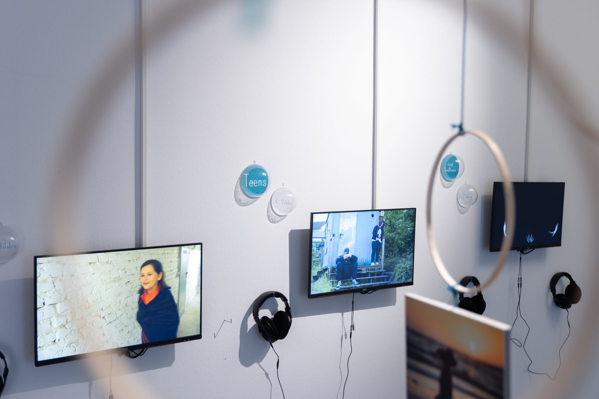 Das Bild zeigt drei Fernseher an einer Wand auf denen die Werke der FreiheitsMOMENTE Ausstellung zu sehen sind.