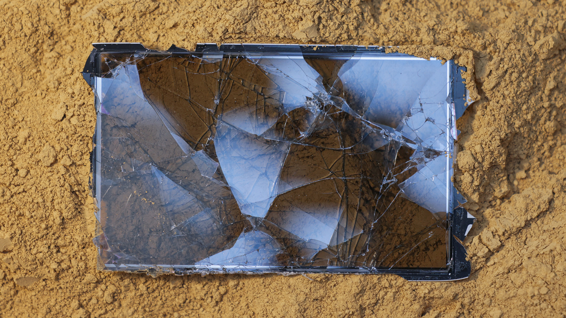 Im Sand liegendes, zerbrochenes Smartphone mit gesplittertem Display; Werk aus der Serie »Mad Rush Extented« von Ana Alenso.