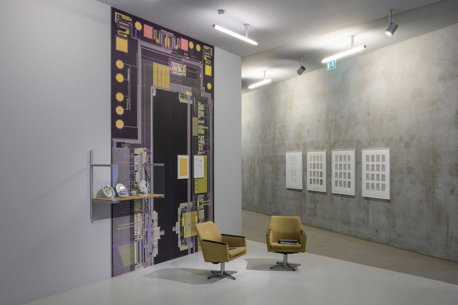 Ausstellungsansicht: Zwei Stühle im Vordergrund, im Hintegrund ein technisches Muster