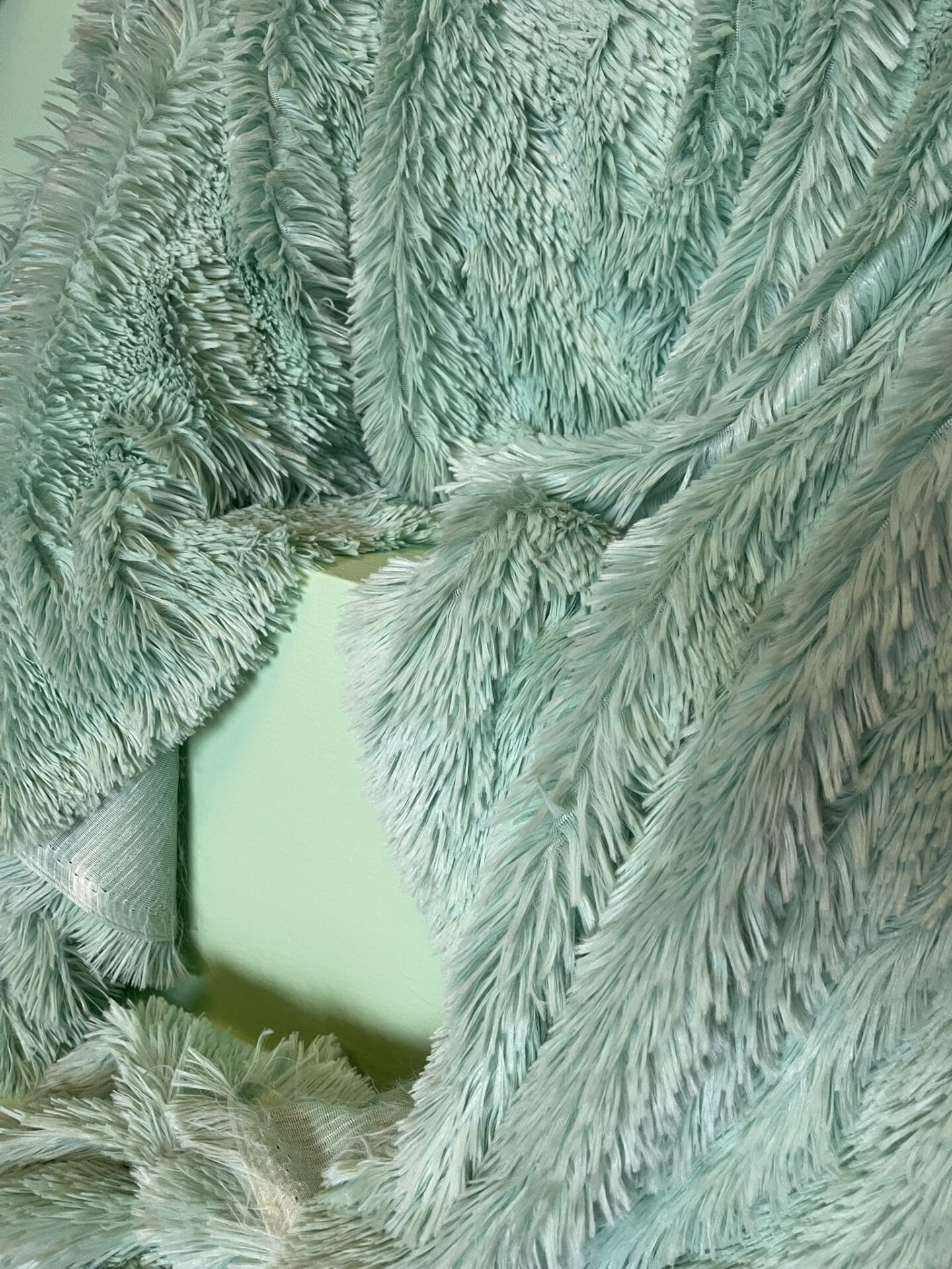Türkisblauer, flauschiger Stoff liegt über einem grünen Würfel.