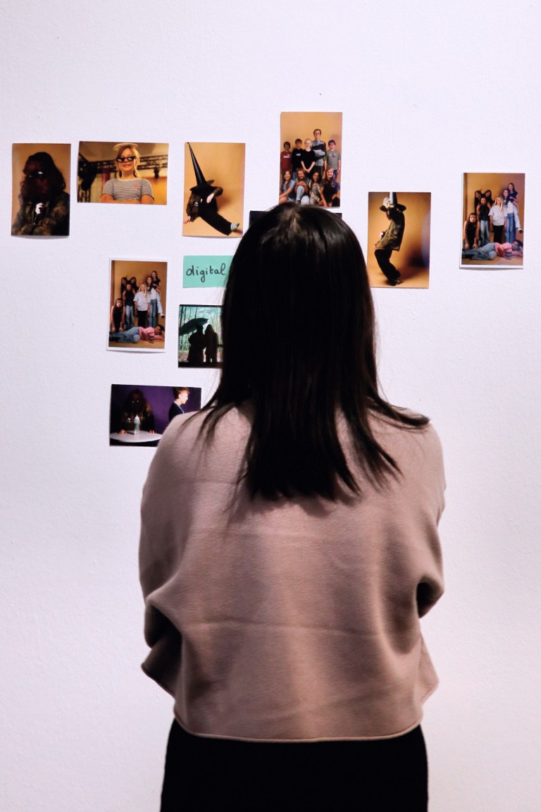Eine Person steht vor einer Wand, an der Fotos hängen.
