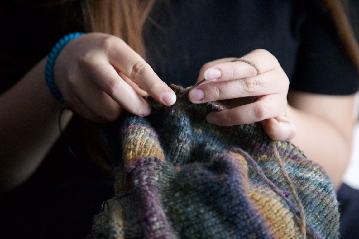 Zwei Hände halten Stricknadeln und stricken.
